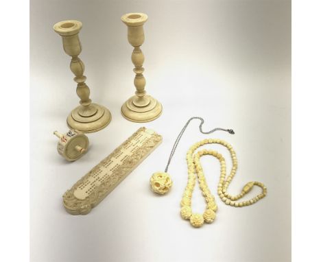 A group of ivory, comprising a pair of candlesticks with turned stems, H14.5cm, a cribbage board with carved border depicting