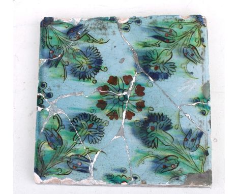 A large 17th century Islamic / Iznic tile decorated with flowers on a turquoise ground, 25 by 25cms (9.75 by 9.75ins) (a/f).