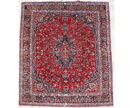 A Persian Meshed woollen hand knotted carpet with foliate design on a red ground, 375 by 295cms (147.5 by 116ins).