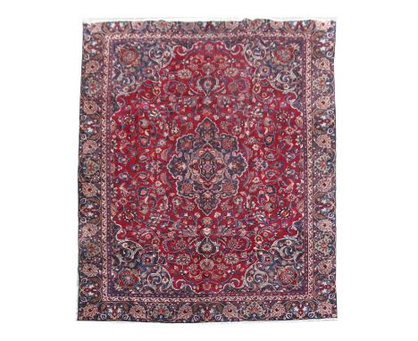 A Persian hand knotted woollen Mashad carpet on a red ground, 360 by 262cms (141.5 by 103ins).