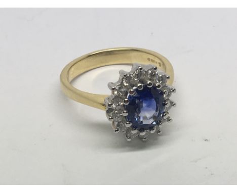 An 18carat yellow gold ring set with a central blue sapphire (enhanced colour) set with a pattern of brilliant cut diamonds. 