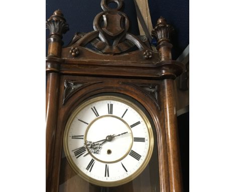 A Vienna wall clock the mahogany case with gothic influence the enamel dial with Roman numerals and visible pendulum.