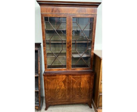 A reproduction mahogany bookcase with a moulded dentil cornice and two glazed doors, the base with two cupboards on splayed b
