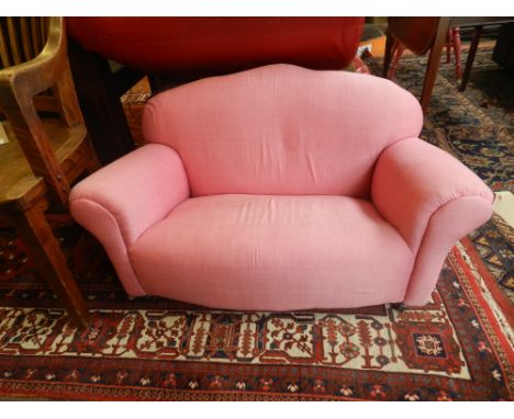 A contemporary child's two seat camel back sofa, upholstered in pink fabric, raised on casters 