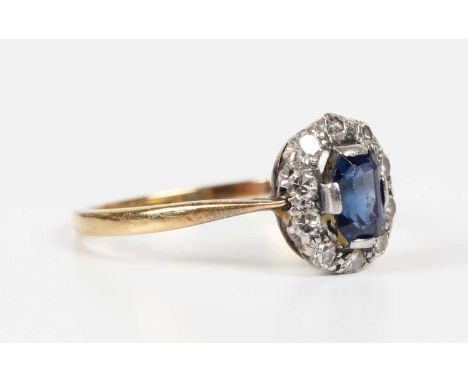 A gold, sapphire and diamond oval cluster ring, mounted with a cut cornered rectangular step cut sapphire within a surround o