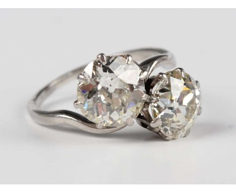 A platinum and diamond two stone ring, claw set with old cut cushion shaped diamonds in a twistover design, unmarked, weight 