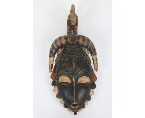 Carved Tribal wooden face mask, 39cm, with long nose, thin eye slits, protruding lips, wearing a horned head dress surmounted