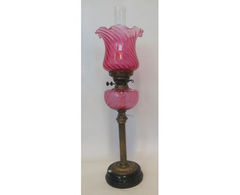 Early 20th century double oil burner lamp with cranberry shade, cranberry reservoir standing on a brass pedestal and ebonised