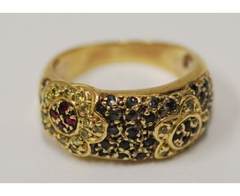 A RING WITH BROAD TOP decorated with two flowers, each set with four tiny red stones and surround of tiny white stones, on a 