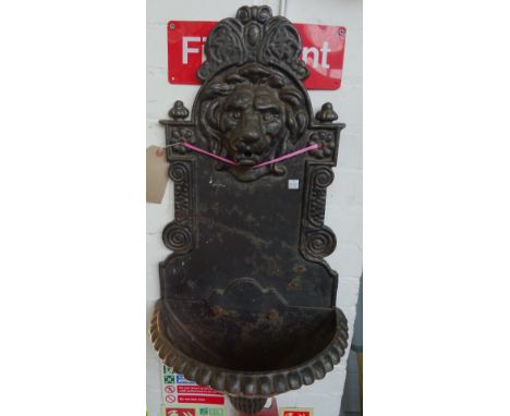 A cast iron wall font, 20th century, with relief cast iron lion's head spout over a fluted demi-lune basin. 80cm high.