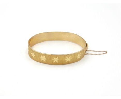 A 9ct gold oval hinged bangle, decorated with a row of bright cut stars, fitted with a safety chain, London 1970, weight 20 g