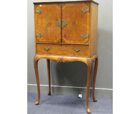 A 1930's walnut cocktail cabinet, the pair of cupboard doors enclosing a mirrored interior with sliding shelf over a single l