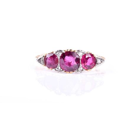 A late Victorian three stone half hoop ruby ring, the mixed circular cut rubies in pierced and engarved claw mounts with rose