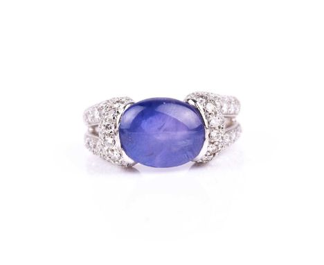 A diamond and tanzanite ring, the double loop shoulders pave-set with round brilliant-cut diamonds, centred with an oval cabo