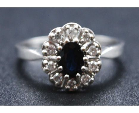 An 18ct white gold, sapphire and diamond oval cluster ring, featuring a centre oval sapphire within a border of ten round bri