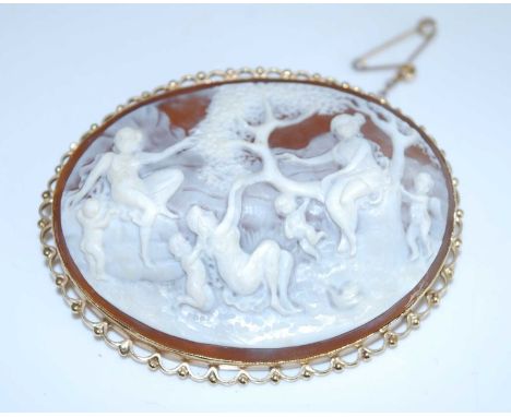 A yellow metal carved shell cameo brooch, depicting a country scene of women and children playing, with a scalloped border an