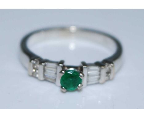 An 18ct white gold, emerald and diamond dress ring, featuring a centre round emerald flanked on either side by three tapered 