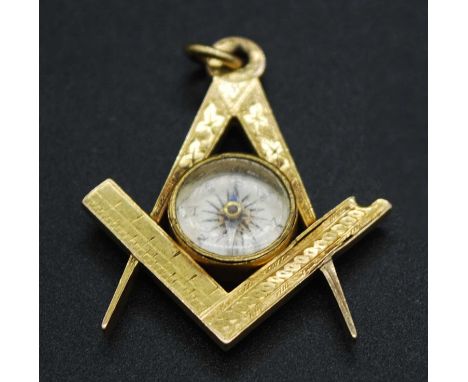 A yellow metal Masonic compass pendant, having bright cut engraved decoration centre set with a glazed compass, unmarked but 