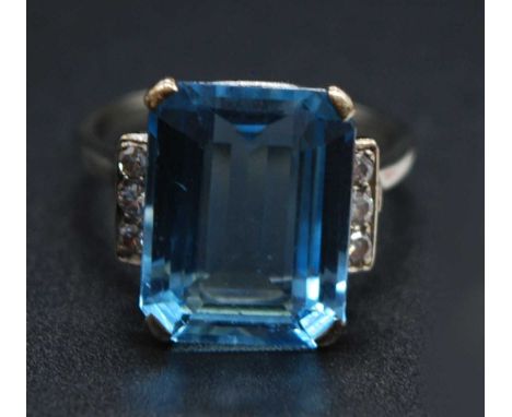 A modern white metal, blue zircon and diamond set dress ring, the four-claw set emerald cut zircon measuring approx 14.5 x 11