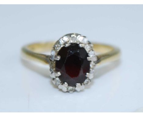 A yellow metal, garnet and diamond oval cluster ring, featuring a centre oval faceted almandine garnet within a border of eig