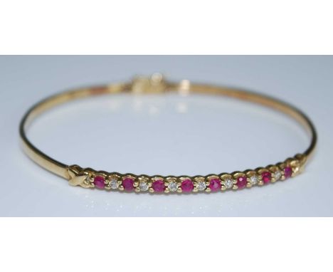 A yellow metal, ruby and diamond oval hinged bangle, featuring eight round faceted rubies alternating with seven round brilli