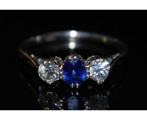 A platinum sapphire and diamond three stone ring, arranged as a central oval cut sapphire, flanked to either side with a sing