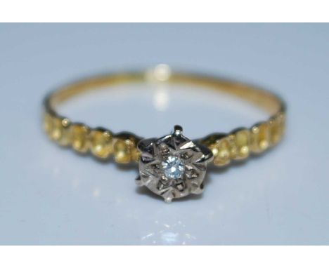 A yellow and white metal diamond single stone ring featuring a round brilliant cut diamond in an illusion setting with textur