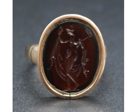 An early 19th century yellow metal red carnelian set signet ring, the oval matrix carved with a standing nude, stamped and te