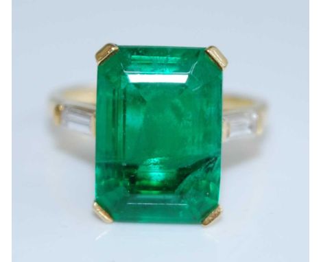 A yellow metal synthetic emerald dress ring, comprising a step cut synthetic emerald in a claw setting with a baguette cut wh