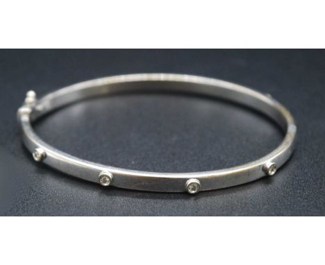 A modern 9ct white gold and diamond highlight set hinged bangle, of hollow square section, illusion set with eight small equi