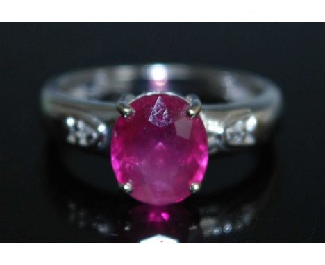 An 18ct white gold, ruby and diamond ring, featuring a centre oval faceted ruby in a four claw setting with a single cut diam