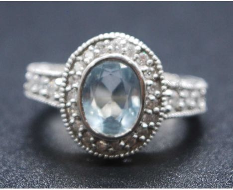 A white metal, aquamarine and diamond oval cluster ring, featuring a centre oval aquamarine within a border of 19 round brill