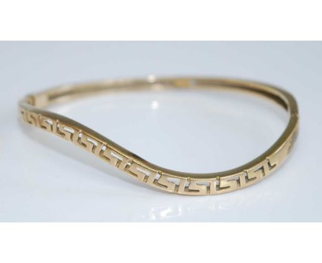A yellow metal hinged bangle, of wavy outline, having Greek Key section, unmarked but tests as approx 14ct, 13.1g, dia.6.3cm