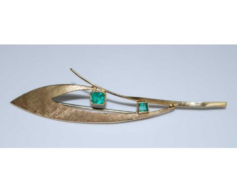 A yellow metal emerald abstract leaf brooch comprising 2 rectangular cut emeralds in bezel settings within a textured openwor