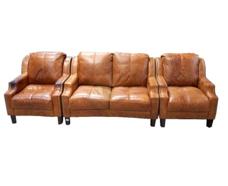 LEATHER THREE PIECE SUITE
comprising two club armchairs and a two seat sofa, all with decorative brass stud detail to the tob