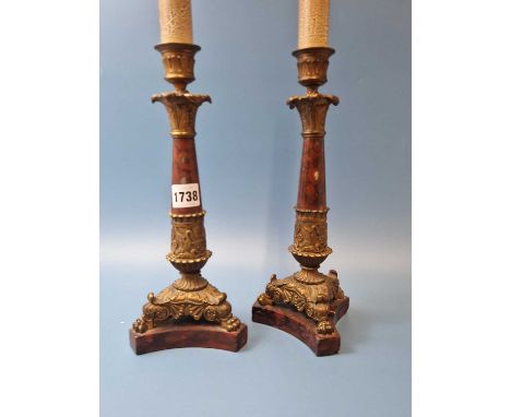A pair of mottled red marble and ormolu candlestick table lamps, the ormolu foliate bases with three paw feet resting on trip