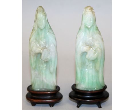 A PAIR OF EARLY 20TH CENTURY CHINESE APPLE-GREEN JADE FIGURES OF GUANYIN, together with fitted wood stands, each carved with 