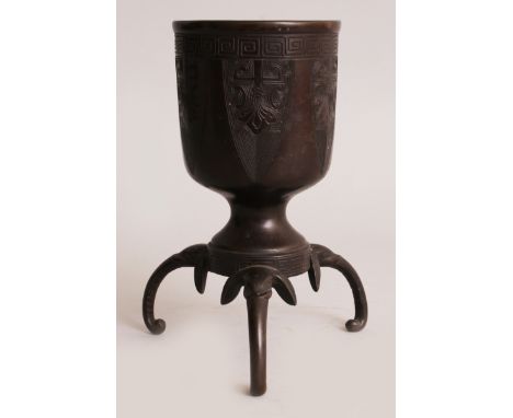 AN ORIENTAL BRONZE TRIPOD STEM CUP, with elephant head and trunk feet, the sides with archaic lappet panels beneath key-fret,