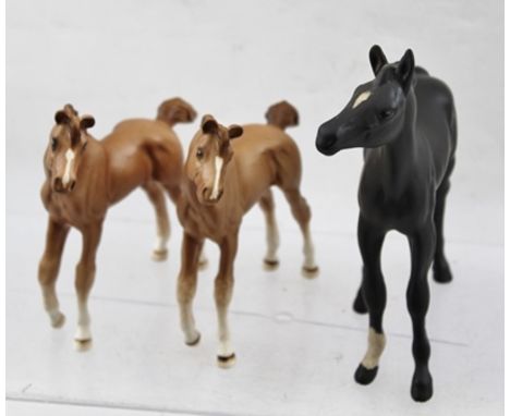A ROYAL DOULTON MATT BLACK FINISHED CERAMIC FOAL with one white sock, together with TWO FROLICKING FOALS finished in a light 