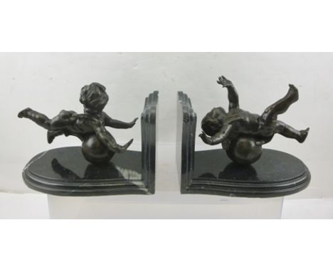 A PAIR OF LATE 20TH CENTURY BRONZE AND MARBLE BOOK ENDS, the black polished forms, mounted with cherubs balancing on balls, e