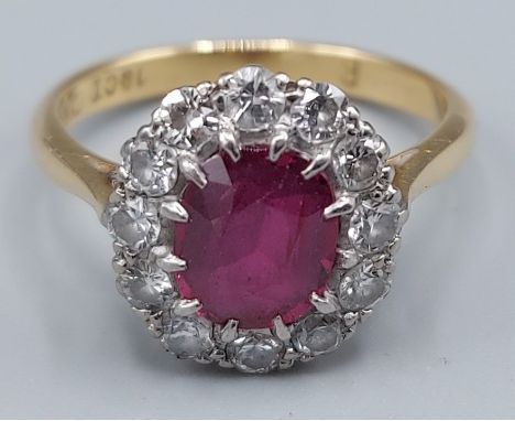 An 18ct gold and platinum Ruby and Diamond cluster ring set with a central oval Ruby surrounded by Diamonds within a pierced 