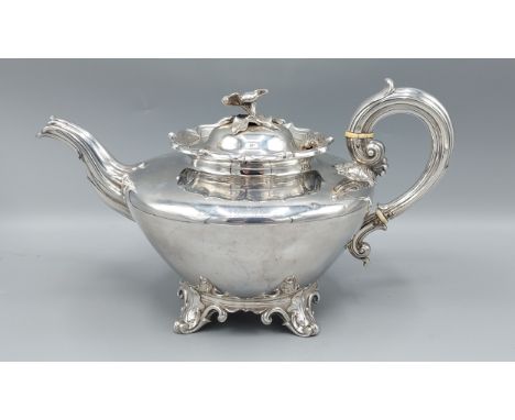 A George IV silver teapot with shaped handle and spout and with foliate cresting upon four scroll feet, London 1836, makers E
