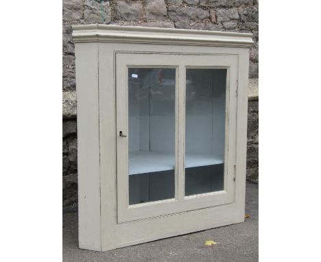 A 19th century countrymade hanging corner cupboard enclosed by a twin rectangular glazed panelled door, revealing a single fi