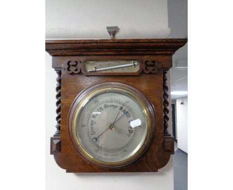 An Edwardian aneroid barometer with silver dial mounted on an oak board with barley twist column supports 