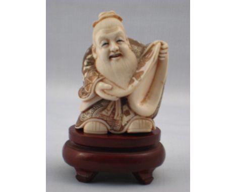 A Chinese ivory figure of a scholar reading a scroll, a beribboned bonnet on his head, hight 6.5cm, hardwood stand. Circa 192