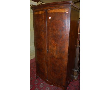 An early 20th century figured walnut feather and crossbanded bowfront double door wardrobe raised on splayed bracket supports