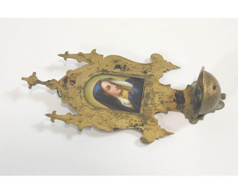 A shaped escutcheon form brass Holy water wall stoup with a central cross to the top and two crooked finials, the centre set 