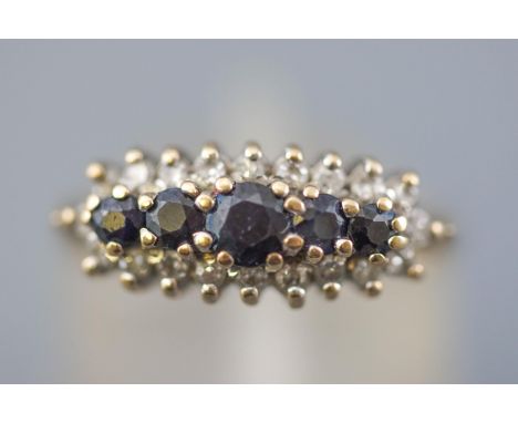 A yellow and white metal cluster ring. Centrally set with five graduated commercial quality dark blue sapphires and surrounde