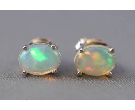 A white metal pair of single stone stud earrings. Each set with an oval cabochon cut Ethiopian welo opal. Post and scroll fit