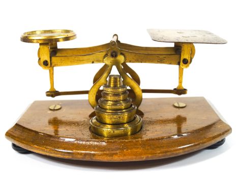 An early 20th century brass set of letter scales with weights, on a mahogany bow fronted stand with bun feet, 19cm wide, toge
